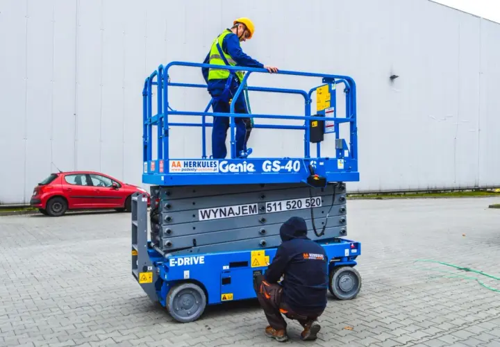 Dwóch pracowników w kaskach i kamizelkach na podnośniku koszowym Genie GS-40.