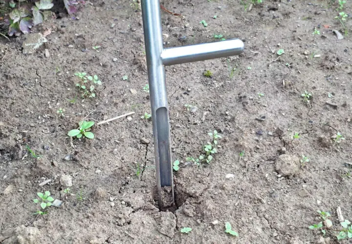 Ein Werkzeug zum Bodenproben ziehen steckt im trockenen Erdreich. Kleine grüne Pflänzchen sprießen zwischen den Rissen im Boden.
