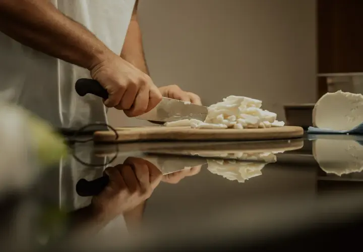 Hände schneiden frischen Käse, eine köstliche fior di latte Alternative, auf einem Holzbrett.