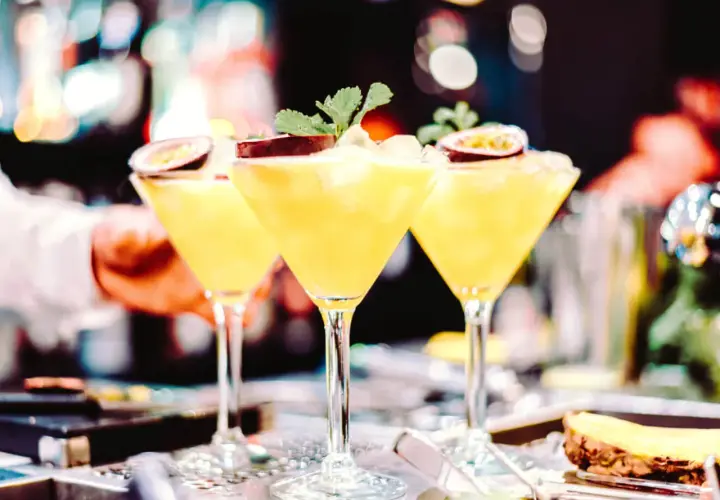 Trzy kieliszki z orzeźwiającą mango margarita, ozdobione połówkami marakui i listkami mięty, gotowe do podania.