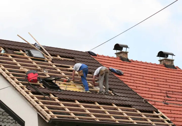 Deux couvreurs travaillent sur une toiture en cours de rénovation, préparant à prolonger un toit existant.