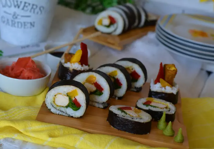 Pyszne sushi z kurczakiem, papryką i mango na desce. Obok miseczka z imbirem i sos sojowy.