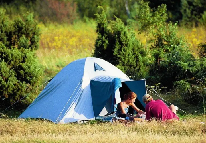 Para spędza czas w namiocie, idealne miejsce na biwak. Otoczeni zielenią i polnymi kwiatami, cieszą się spokojem natury.