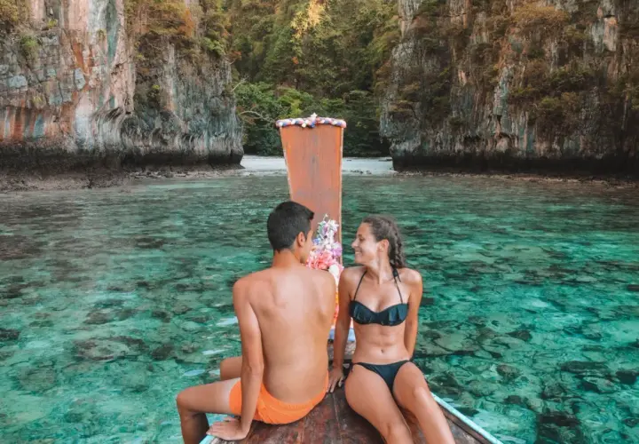 Pareja en bote de madera, aguas cristalinas y acantilados. Un destino ideal para saber donde viajar en enero.