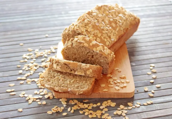 Pane proteico integrale, cosparso di fiocchi d'avena, affettato su un tagliere di legno.
