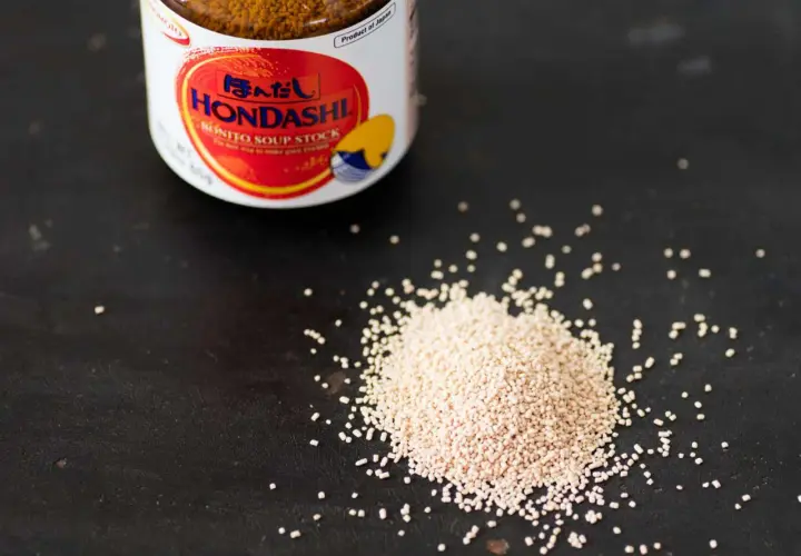 A jar of Hondashi soup stock sits next to a pile of granules. This image helps visualize the dashi powder to water ratio for perfect Japanese broth.