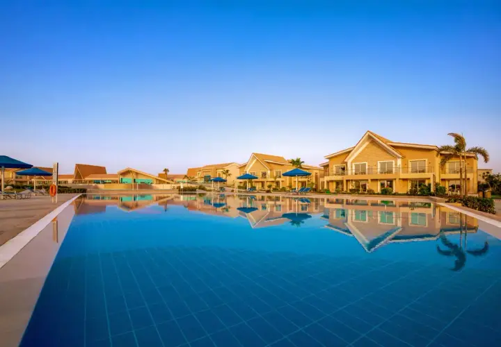 Basen hotelowy w Pickalbatros Sea World Marsa Alam z odbijającymi się w wodzie budynkami i palmami.