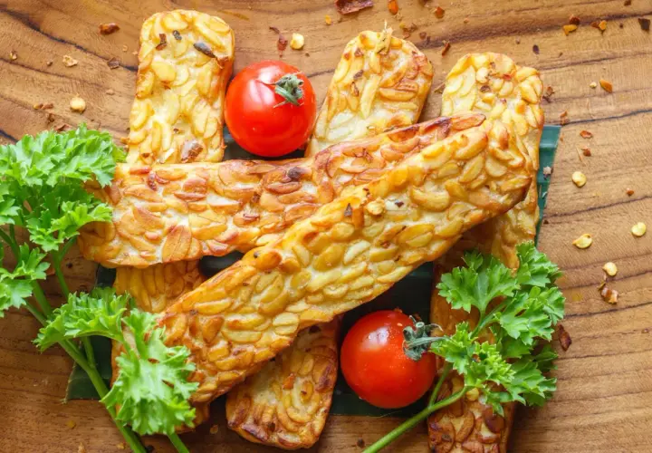 Złociste kawałki tempeh, smażone na złoto, z pomidorkami i natką pietruszki. Tempeh co to? To pyszna, roślinna alternatywa!