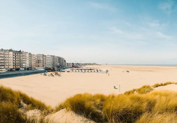 Breiter Sandstrand mit Dünen und Strandkörben in Belgien, Knokke. Lange Häuserzeile am Boulevard.
