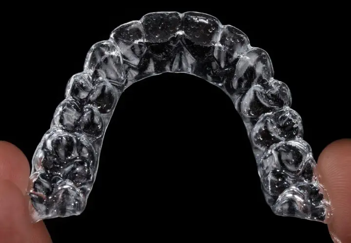 Przezroczysty aparat Invisalign, trzymany palcami, z widocznymi indywidualnymi nakładkami na zęby.