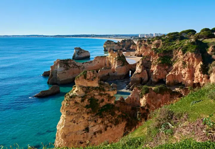 Acantilados dorados y mar turquesa en las **playas de Portugal**. Un paisaje idílico con formaciones rocosas y vegetación exuberante.