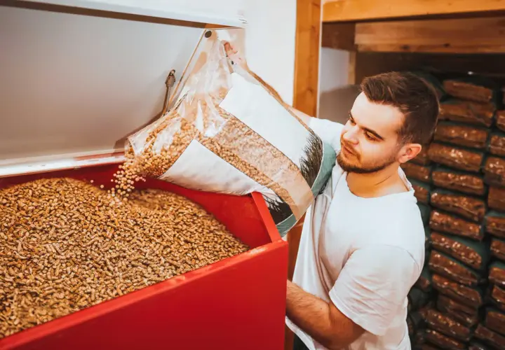 Mann füllt Holzpellets in einen Behälter. Die Pellets preisentwicklung ist ein wichtiges Thema für Heizungsbesitzer.