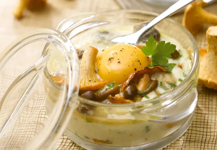 Un œuf au plat, entouré de champignons et de persil, dans un ramequin en verre. Un plat savoureux d'œufs au four.