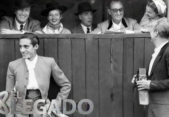 Un torero posa sonriente, mientras un fotógrafo captura el momento. Detrás, un grupo de espectadores, evocando la época de los toreros de los 90.