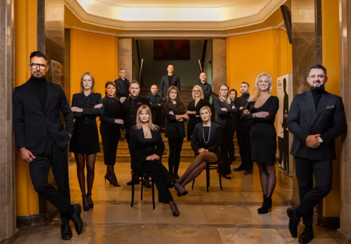 Grupa profesjonalistów w czarnych strojach pozuje w eleganckim wnętrzu.