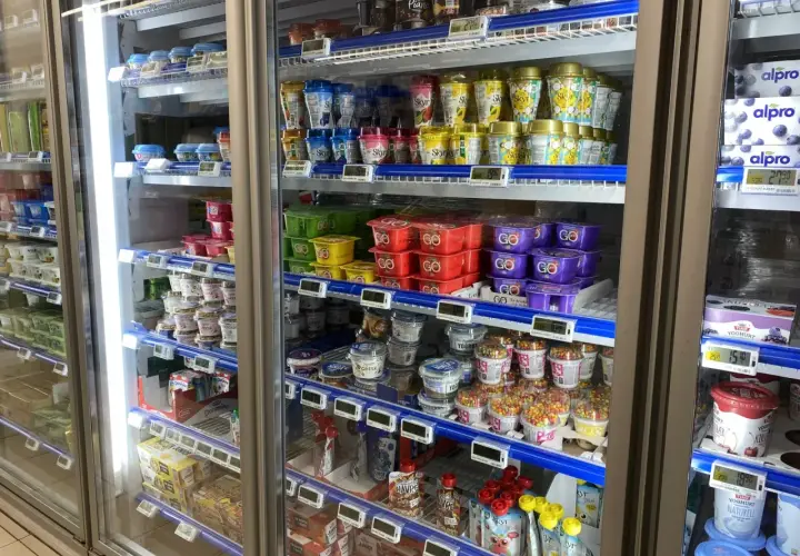 W lodówce w Norwegii widać jogurty i desery. Ceny w sklepach są widoczne na etykietach, np. 27,90 za jogurt.