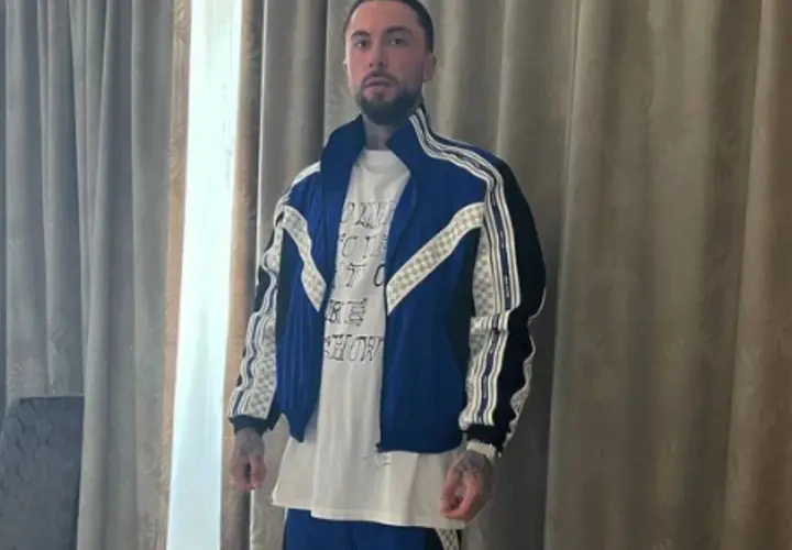 Malik Montana w niebieskiej kurtce i białej koszulce, gotowy na spotkanie z malik montana dzieci.