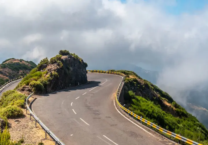 Curva pronunciada en la **ruta N2 Portugal**, bordeada por barrancos y vegetación exuberante, con nubes bajas cubriendo el paisaje montañoso.