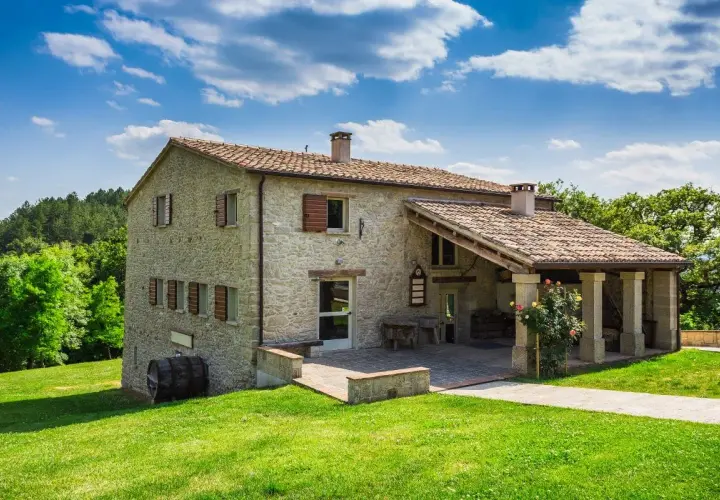 Belle ferme en pierre, résultat d'une rénovation réussie, nichée dans un paysage verdoyant sous un ciel bleu.