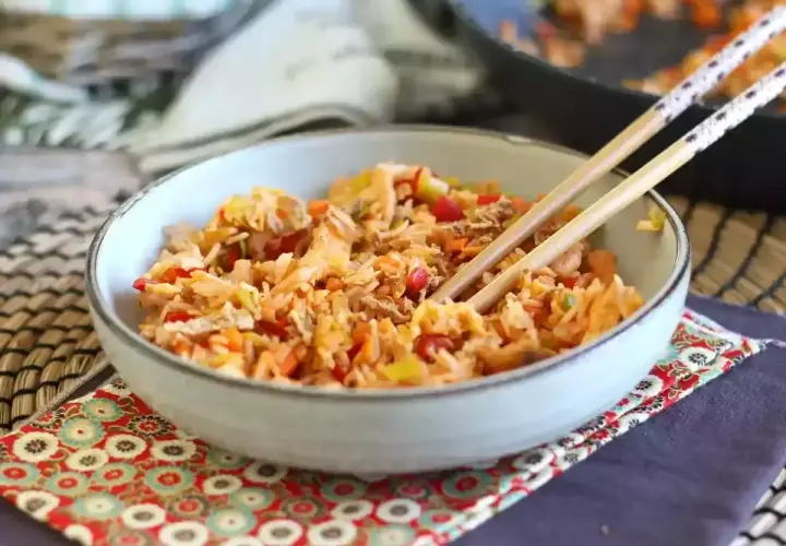 Miseczka pełna aromatycznego nasi goreng z warzywami i kawałkami kurczaka, gotowa do jedzenia pałeczkami.