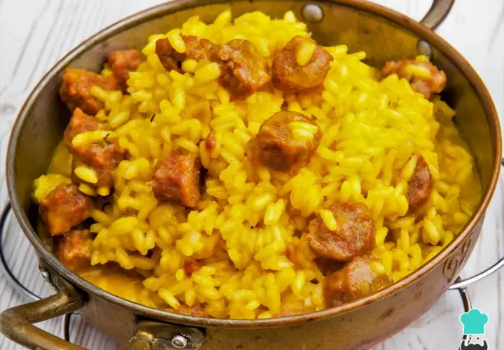 Arroz a la milanesa, un plato amarillo vibrante con trozos de salchicha, servido en un cuenco de cobre.