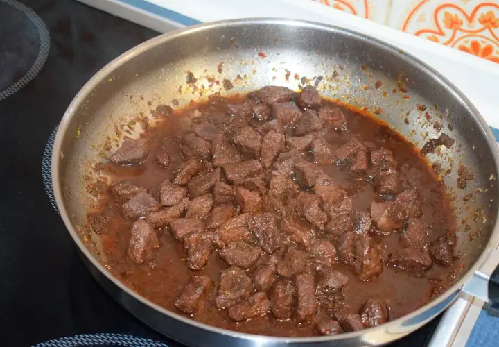 Kawałki wieprzowiny duszą się w sosie, co jest kluczowe, jak zmiękczyć twarde mięso wieprzowe na gulasz naturalnymi metodami.