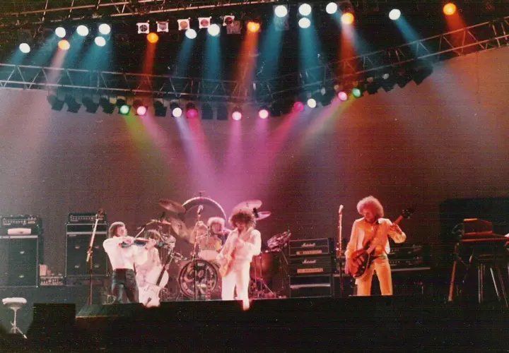 Zespół Electric Light Orchestra na scenie, grający największe przeboje. Kolorowe światła sceniczne podkreślają atmosferę koncertu.