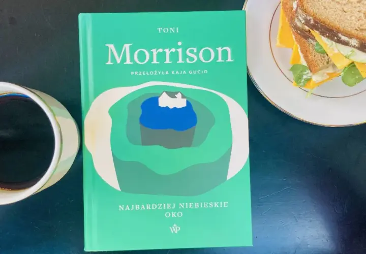 Zielona okładka książki Toni Morrison "Najbardziej niebieskie oko" leży obok filiżanki kawy i kanapki.