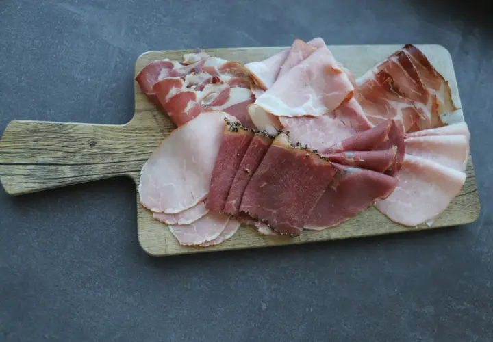 Holzbrett mit verschiedenen Aufschnittsorten, darunter zarter **prosciutto crudo**, Schinken und Rindfleisch.