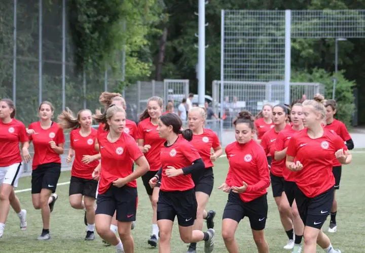 Eine Gruppe junger Fußballerinnen der u17 Juniorinnen im roten Trikot läuft auf einem Kunstrasenplatz.