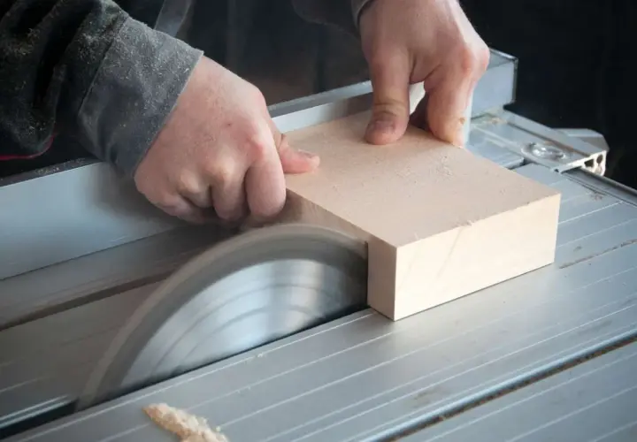 Mani esperte guidano un pezzo di legno su una sega circolare, uno degli attrezzi per tagliare il legno con precisione, per creare un taglio netto.