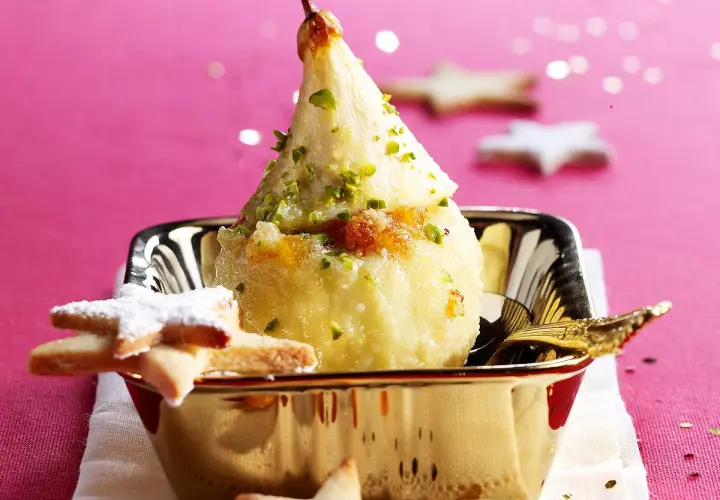 Poire pochée, garnie de pistaches et de miettes de biscuit, servie dans un bol doré. Une idée gourmande pour une recette chartreuse.