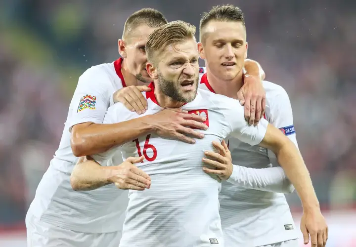Trzech kapitanów reprezentacji Polski w białych strojach świętuje bramkę.