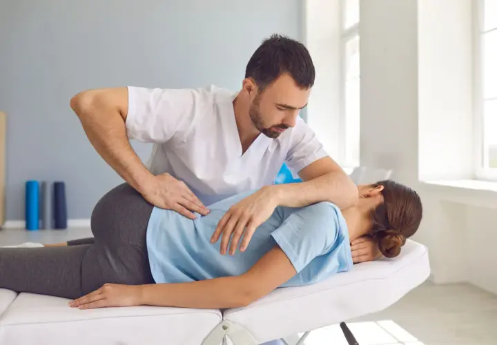 Fizjoterapeuta wykonuje terapię manualną kręgosłupa u pacjentki leżącej na kozetce.