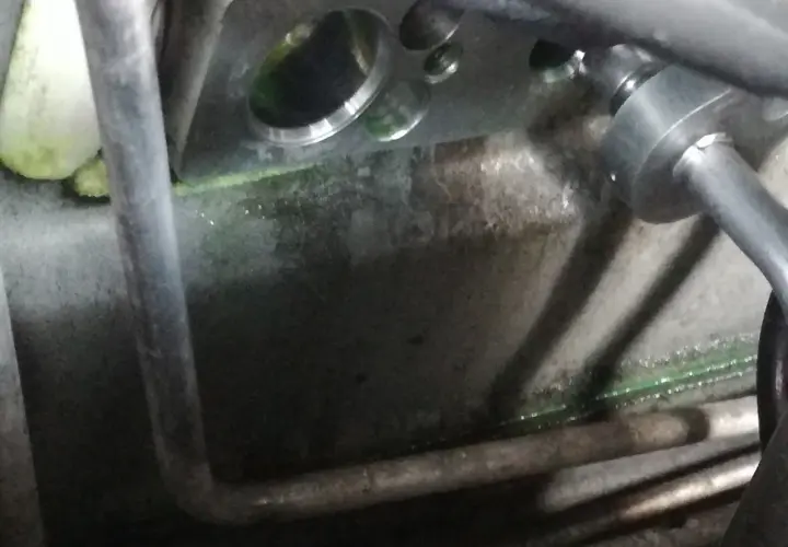Metalowy blok z otworami, gdzie jest zawór rozprężny klimatyzacji. Widać zielony płyn i rury.