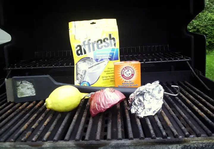 Sur la grille barbecue, un citron, un oignon, du papier aluminium, un nettoyant pour lave-vaisselle et du bicarbonate de soude.