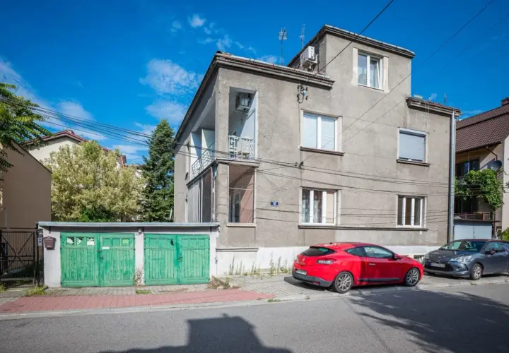 Szare apartamenty Bandtkiego z zielonymi garażami i czerwonym samochodem na tle błękitnego nieba.