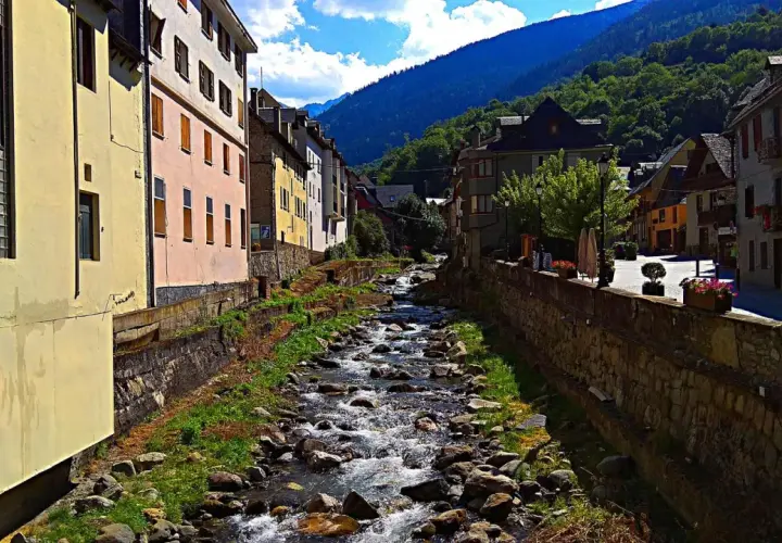Un río serpentea entre casas de colores y montañas verdes. La **altitud vielha** se siente en el aire fresco y la vista panorámica.