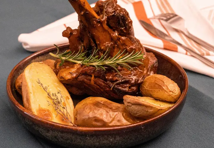 Un plat appétissant de souris d'agneau confite, tendre et savoureuse, accompagnée de pommes de terre rôties et d'une touche de romarin frais.
