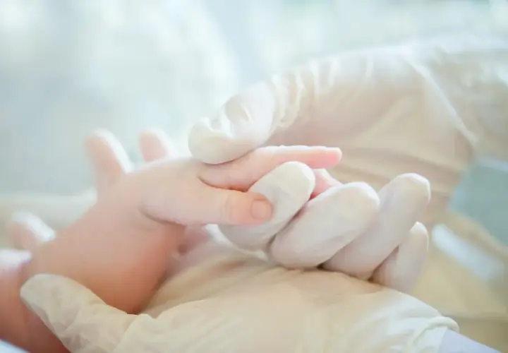 Mani guantate che tengono delicatamente un neonato, un simbolo di cura e attenzione per i possibili danni neurologici da parto.