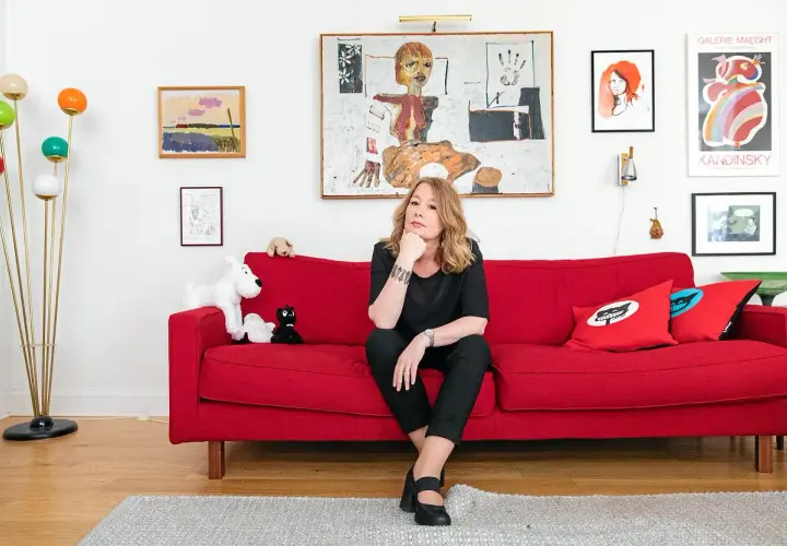 Åsa Linderborg sitter på en röd soffa, omgiven av konst och leksaker som påminner om barn.