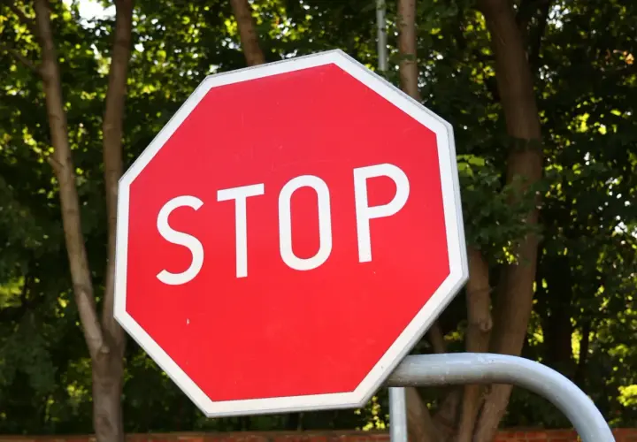 Ośmiokątny czerwony znak stop z białym napisem "STOP" na tle zielonych drzew.