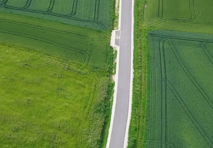 Asfaltowa droga wewnętrzna przecina zielone pola uprawne.