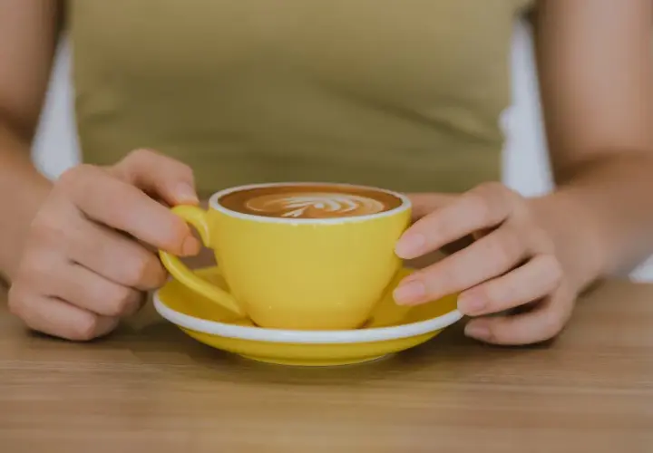 Po treningu zasłużona kawa. Jasnożółta filiżanka z latte art na drewnianym blacie.