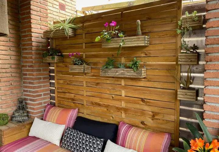 Un rincón acogedor con cojines coloridos y una pared de madera con macetas colgantes, perfecta para tu **diy decoracion** exterior.