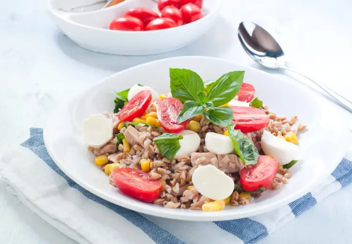 Deliziosa insalata di orzo con tonno, pomodorini, mais e mozzarelline, guarnita con basilico fresco. Un piatto completo e colorato.