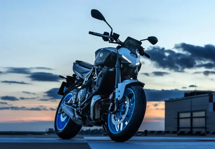Yamaha MT-07 gotowy do nocnej jazdy. Niebieskie felgi lśnią w blasku zachodzącego słońca.