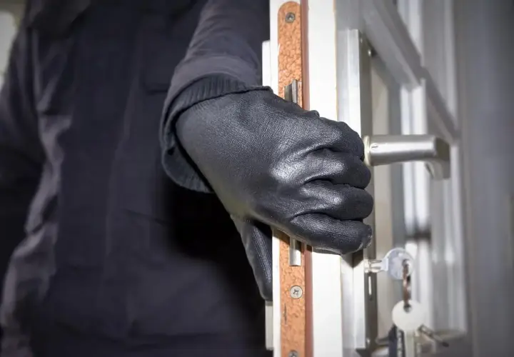 Ręka w czarnej rękawiczce otwiera drzwi, klucze wiszą na zamku. Sen o włamanie może oznaczać niepokój.