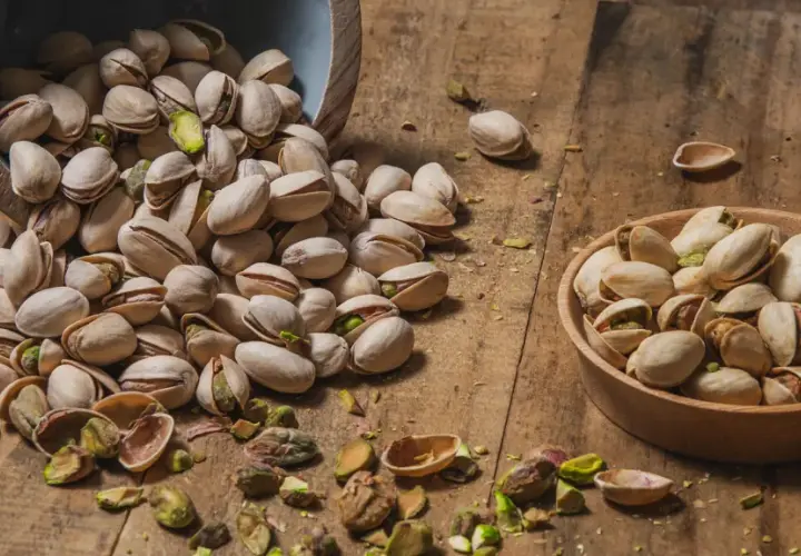 Pistacchi in una ciotola e sparsi su un tavolo di legno. Scopri le incredibili pistacchi proprietà per la tua salute.