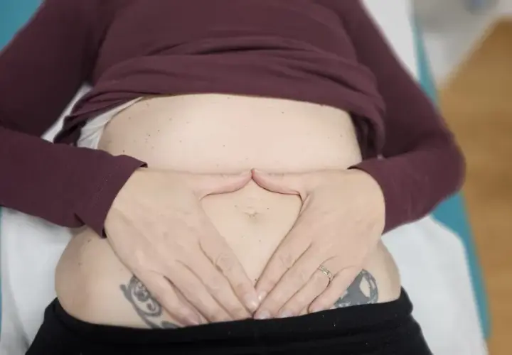 Manos sobre el abdomen, sintiendo el dolor de espalda por gases.